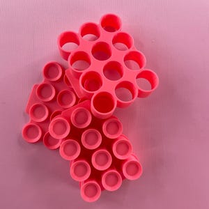 May include: Three pink silicone pop-it fidget toys stacked on top of each other. The top toy has a hexagonal shape with 18 circles. The middle toy has a hexagonal shape with 12 circles. The bottom toy has a rectangular shape with 18 circles.