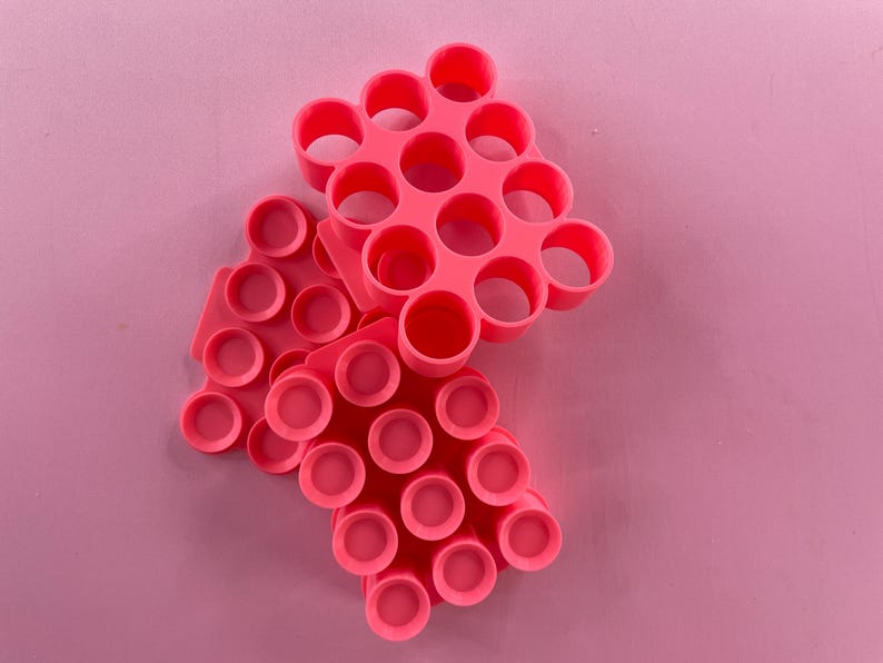 May include: Three pink silicone pop-it fidget toys stacked on top of each other. The top toy has a hexagonal shape with 18 circles. The middle toy has a hexagonal shape with 12 circles. The bottom toy has a rectangular shape with 18 circles.