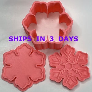 May include: Three pink plastic cookie cutters shaped like snowflakes. The largest cutter is a snowflake with six points and a hollow center. The two smaller cutters are solid snowflakes with six points.