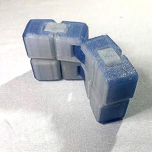 May include: Two blue and gray fidget cubes are shown. The cubes are made of a translucent material, with a textured surface. The cubes are interlocked, and appear to be in motion. The cubes are on a white surface.