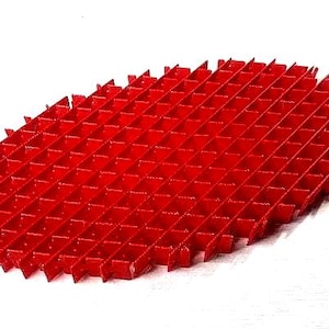 May include: A bright red, oval-shaped plastic grid with a repeating square pattern. The grid is made of intersecting vertical and horizontal bars, creating a series of small, open squares. The edges are slightly raised and angled, giving it a textured appearance.