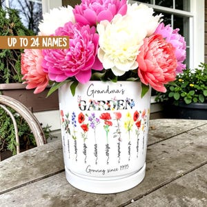 Puede incluir: Una maceta de cerámica blanca con el texto "Grandma's GARDEN" y las palabras "Growing since 1995". La maceta está llena de peonías rosas, blancas y rojas. La maceta tiene un diseño floral y las palabras "UP TO 24 NAMES".