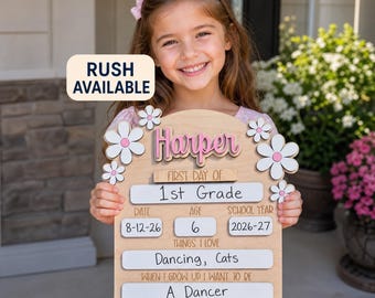 May include: A wooden first day of school sign featuring the name Harper in pink, white flower cutouts, and white rectangular spaces for grade, date, age, school year, interests, and future goals. The text RUSH AVAILABLE is printed in a box.