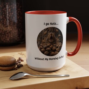 Puede incluir: Taza de café de cerámica blanca con borde y asa rojos. La taza presenta un gráfico de una ardilla rodeada de nueces con el texto "I go Nuts... Without My Morning Coffee!"
