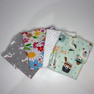 Può includere: Cinque quadrati di tessuto con motivi diversi. Un quadrato ha uno sfondo bianco con pois neri. Un quadrato ha uno sfondo grigio con unicorni bianchi. Un quadrato ha uno sfondo bianco con fiori colorati. Un quadrato ha uno sfondo bianco con fiori colorati e una grande margherita gialla. Un quadrato ha uno sfondo blu chiaro con pois neri e un motivo di orsi che indossano cappelli.