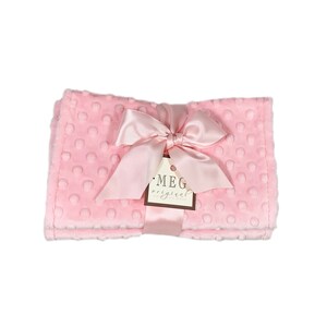 May include: A soft pink baby blanket with a textured dot pattern. The blanket is tied with a satin ribbon and a tag that reads "MEG original hand made". The blanket is folded and ready to be gifted.