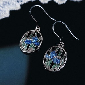 May include: A pair of silver earrings with blue and green enamel iris flower designs.