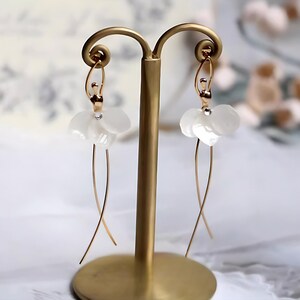 Dainty Pressed Flower Ballerina Earrings in white, displayed on a gold stand. A whimsical jewelry piece for a dancer girl.