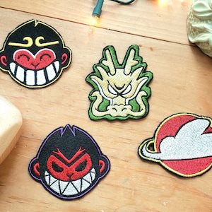 Peut inclure: Quatre patchs brodés à repasser. L'un est un dragon vert aux yeux jaunes, l'autre est un nuage rouge et blanc avec un anneau jaune, et les deux autres sont des visages de singe noirs et rouges avec des dents blanches.