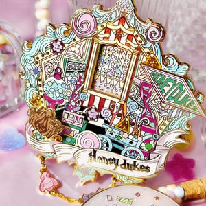 Può includere: Spilla smaltata colorata con un design stravagante con un treno, dolci e la scritta "Honeydukes". La spilla ha un bordo dorato ed è decorata con vari colori, tra cui rosa, blu e verde. Oggetto da collezione.