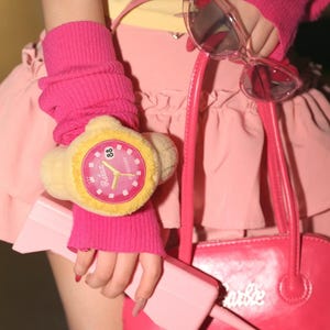 May include: A vibrant pink handbag, sunglasses, and a plush watch are shown. The watch has a yellow face with the word "Relax" and the number "88". The sunglasses have clear frames. The handbag is bright pink with the word "Barbie" on it.