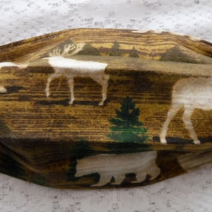 May include: A brown, green and white face mask with a woodland pattern featuring moose, deer and trees.