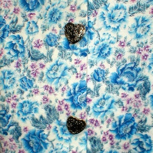 May include: White fabric with a blue floral pattern and two gold heart-shaped buttons.