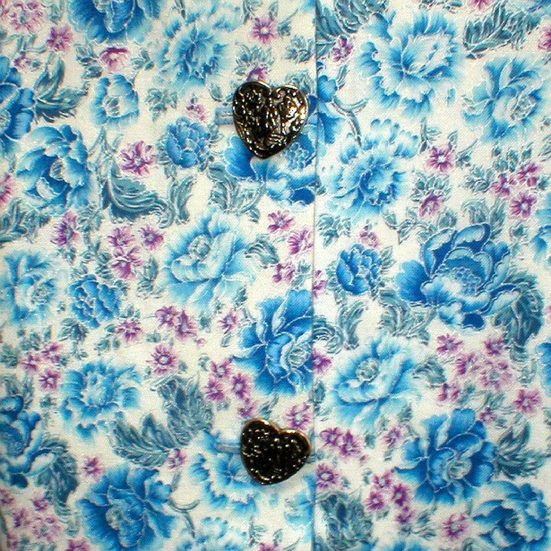 May include: White fabric with a blue floral pattern and two gold heart-shaped buttons.
