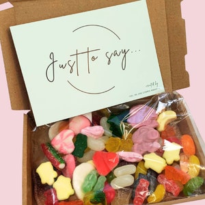May include: A cardboard box with a light green card that says "Just to say..."  The box is filled with a variety of colourful sweets, including gummy bears, jelly beans, and other assorted candies.