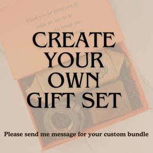 Może przedstawiać: Otwarty, brzoskwiniowy karton prezentowy z napisem "CREATE YOUR OWN GIFT SET" dużymi czarnymi literami. Wewnątrz widoczna jest beżowa kosmetyczka, zwinięty pasek i mała karta. Pudełko zawiera r&oacute;wnież tekst.
