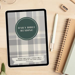 May include: A digital tablet with a gray and white plaid background. The text "DAILY BIBLE READING" is in a green circle on the screen. The text "HOW I DO LOVE YOUR LAW/I PONDER OVER IT ALL DAY LONG, PSALM 119:97" is at the bottom of the screen.