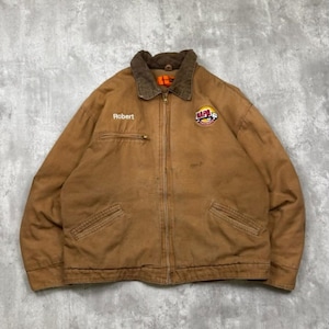 Peut inclure: Une veste de travail en toile beige avec un col en velours côtelé marron, une fermeture éclair frontale intégrale et deux poches inclinées. La poitrine porte le nom Robert brodé et un écusson NAPA circulaire avec un camion.
