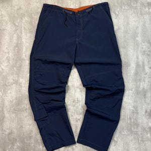 May include: Navy blue cargo pants with orange interior waistband and drawstring. The pants have multiple pockets and reinforced stitching. The pants are made of a lightweight material.