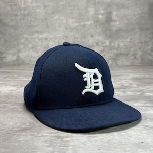 May include: A navy blue baseball cap featuring a white embroidered "D" logo. The cap has a curved peak and a structured crown. This classic hat is suitable for casual wear and measures approximately 20 cm in diameter.