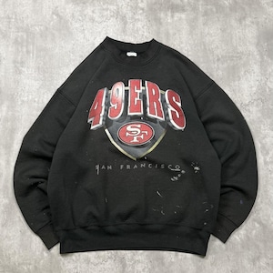 May include: A black long-sleeve crewneck sweatshirt featuring a large graphic on the chest with the red and white text 49ERS above a shield logo containing the letters SF. The text SAN FRANCISCO is printed in white below the shield logo.