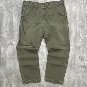 Op de afbeelding: Olijfgroene werkbroek met meerdere zakken en een rechte pijp. De broek vertoont tekenen van slijtage, met zichtbare vlekken en vervaging. De broek is gemaakt van een duurzame stof.