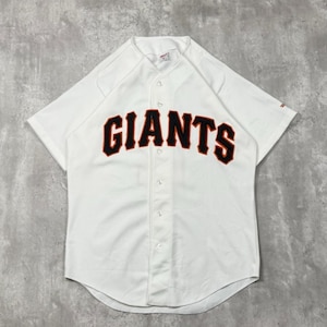 Peut inclure: Un maillot de baseball blanc à manches courtes avec le mot GIANTS inscrit en lettres noires bordées d'orange sur la poitrine. Cette chemise boutonnée présente un ourlet arrondi, un col classique et un petit écusson sur la manche droite.