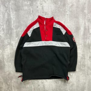 以下が含まれることがあります： 黒、赤、シルバーのフリースプルオーバー。ハイカラーとボタン留めが特徴です。赤い上部、黒の中央部、シルバーのアクセントを組み合わせたカラーブロックデザイン。ブランド名は胸元に表示されています。