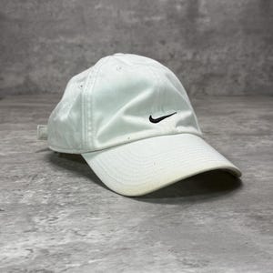Può includere: Un cappellino da baseball bianco con un piccolo logo Nike nero ricamato al centro sul davanti. Il cappellino presenta una corona strutturata, una visiera curva e una chiusura con cinturino in tessuto sul retro, dal design sportivo ed essenziale.