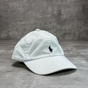 Peut inclure: Casquette de baseball bleu clair avec une visière incurvée. Le chapeau présente un logo brodé bleu foncé d'un joueur de polo sur le devant. Fabriqué en tissu doux et texturé.