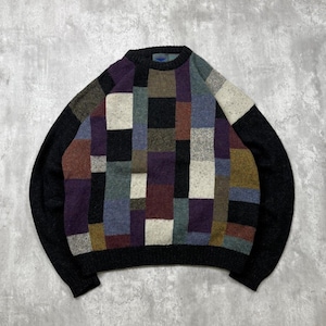 May include: A crew neck sweater with a patchwork design. The sweater features a pattern of various colored squares, including black, purple, white, and brown. The sleeves and collar are solid black.