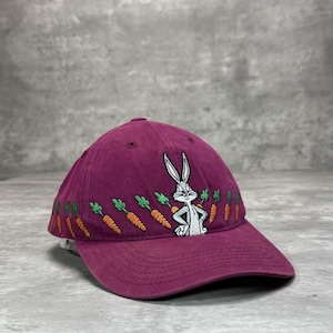 Op de afbeelding: Bordeaux baseballpet met geborduurde Bugs Bunny en wortelen. De pet heeft een gebogen klep en een klassiek zes-panelen ontwerp. De Bugs Bunny-afbeelding is wit en grijs.