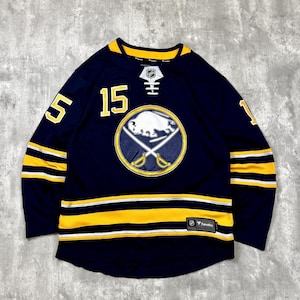 May include: A navy blue hockey jersey featuring the Buffalo Sabres logo in the center, the number 15 in yellow on the chest, and yellow and white stripes on the sleeves and hem. The jersey includes a lace-up collar and a Fanatics brand tag.