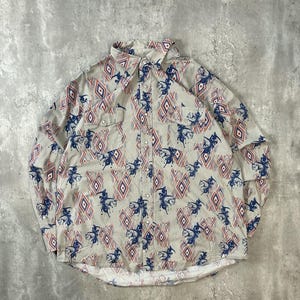 May include: A long-sleeved button-down shirt with a cream-colored background. The shirt features a repeating pattern of blue cowboys on horses and red and blue diamond shapes. The shirt has two chest pockets and silver-colored buttons.