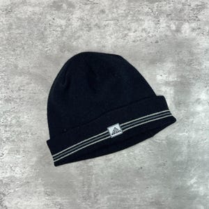 May include: Black knit beanie with two gray stripes and a small white Adidas logo. The hat is a classic winter accessory, suitable for cold weather. The beanie is made of a soft, warm material.
