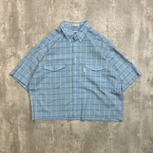 Peut inclure: Une chemise boutonnée à manches courtes bleu clair avec un motif à carreaux bleu clair et vert. La chemise a deux poches de poitrine et une petite étiquette blanche. Le col est boutonné.