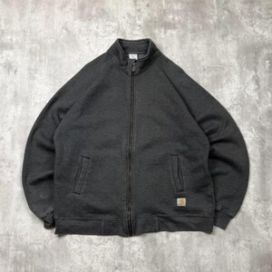 Könnte beinhalten: Eine anthrazitfarbene Reißverschlussjacke mit Stehkragen, langen Ärmeln mit gerippten Bündchen und zwei vorderen Leistentaschen. Ein kleines rechteckiges Carhartt-Markenetikett ist unten links in der Nähe des Saums aufgenäht.