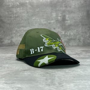 May include: Olive green baseball cap with a black brim. Features an embroidered B-17 bomber design, the text "B-17", and a white star. The cap has a curved brim and a classic six-panel design.