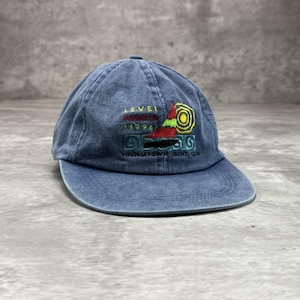 May include: A blue baseball cap with a faded finish featuring an embroidered design of a sailboat, a yellow sun, and the text LEVEL REGATTA 1996 YOUNGSTOWN YACHT CLUB. The cap has a curved brim and a six-panel construction with a button on the top.