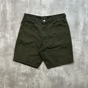 May include: Dark olive green denim shorts with a button closure and pockets. The shorts have a classic five-pocket design and a straight leg fit. The garment is made of a sturdy denim material.