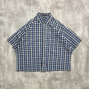 May include: A short-sleeved button-down shirt with a blue and white checkered pattern. The shirt has a classic collar and a chest pocket. The fabric appears to be lightweight, suitable for warm weather.