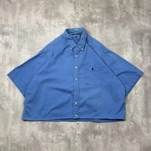 Pode incluir: Uma camisa de manga curta com botões em um tom azul médio sólido. A camisa apresenta uma gola pontiaguda, uma carcela de botões frontal e um bolso único no peito no lado esquerdo com um pequeno logotipo escuro bordado de um cavaleiro.