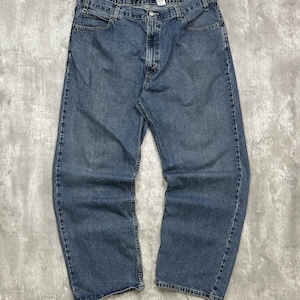 May include: A pair of medium-wash blue denim jeans featuring a classic five-pocket design, a button and zipper fly closure, belt loops, and a straight-leg cut. The jeans have a visible yellow brand label on the interior waistband.