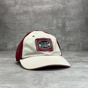 May include: A baseball cap with a maroon brim and top, and a cream-colored front panel. The cap features a rectangular patch with the text "NASCAR NEXTEL CUP SERIES" in black and white.