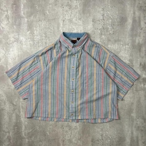 Può includere: Una camicia a maniche corte con bottoni e righe verticali rosse, gialle, verdi e blu. La camicia ha un colore di base azzurro e un colletto blu. La camicia è tagliata in vita.