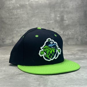 May include: Black baseball cap with a green brim. The cap features a green and white logo of a hop plant with a blue accent. The top of the cap has green stitching.