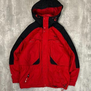 Peut inclure: Veste à capuche rouge et noire avec cordon de serrage et plusieurs poches. La veste a une capuche noire et des empiècements noirs sur les épaules et les poches. Fabriquée dans un matériau durable.