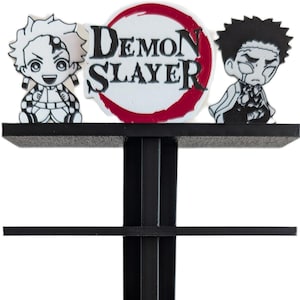 Peut inclure: Présentoir noir avec le logo "Demon Slayer" et des figurines de personnages. Le présentoir comporte plusieurs étagères avec des compartiments rectangulaires. Le logo est blanc avec un bord rouge. Les figurines sont en noir et blanc.
