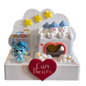 May include: A white Care Bears playset featuring a castle with blue turrets, yellow stars, and a heart-shaped doorway. A Funko Pop figure of a blue Care Bear wearing a nightcap is included. A red heart with "Care Bears" text is in the foreground.