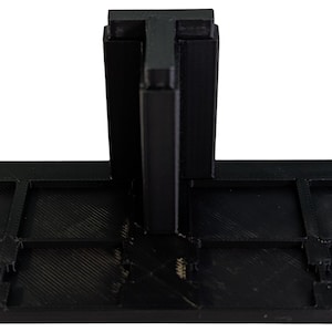 May include: A black rectangular base with a grid of eight recessed square compartments and a central vertical T-shaped support structure extending upward. The object features a matte finish and a rigid, geometric construction throughout its design.
